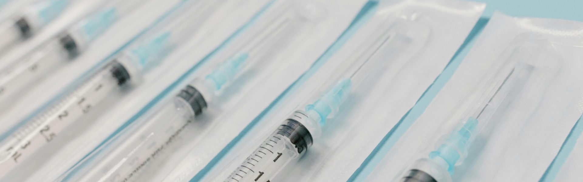 Close-up of sterile syringes aligned on a light blue surface, highlighting medical equipment.